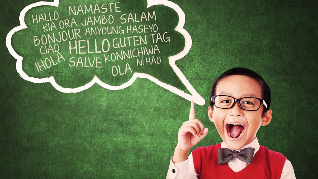 A Young Boy With Hello written in 14 Languages in a Word Bubble on a Green Chalkboard.